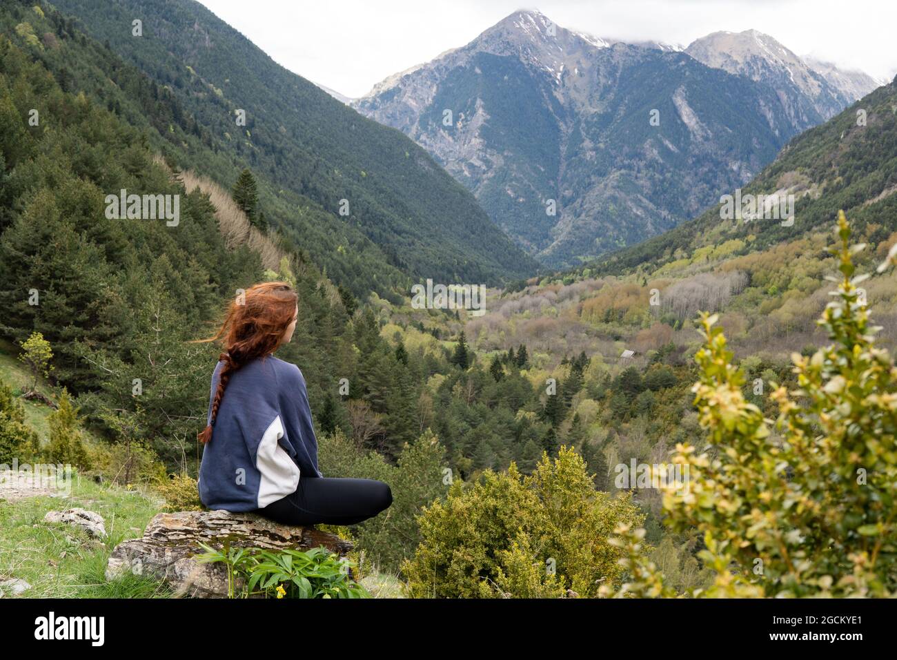 Back view of anonymous female hiker sitting on stone and enjoying scenery of Pyrenees mountain range Stock Photo