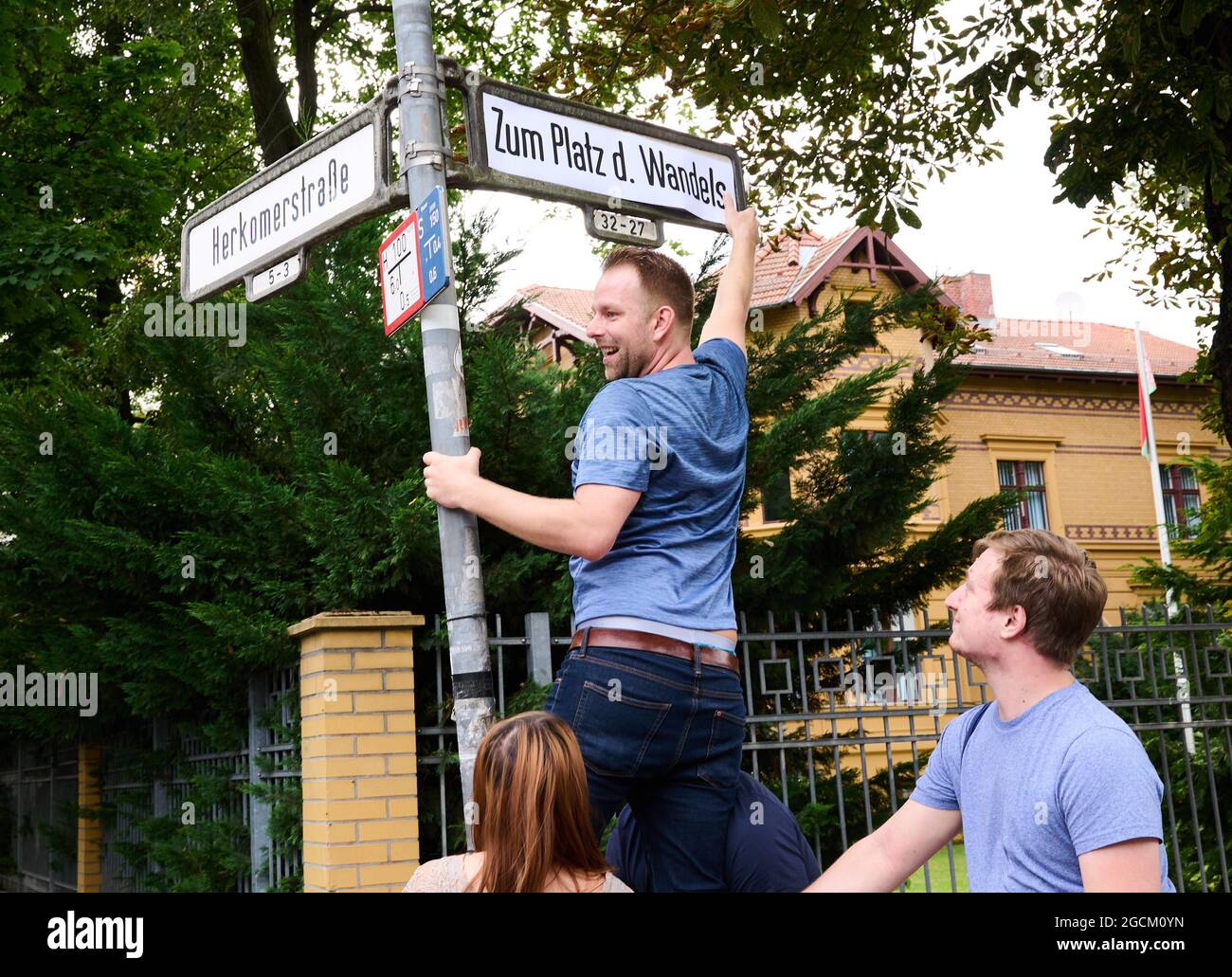 Berlin, Germany. 09th Aug, 2021. Alexander Freier-Winterwerb (M), SPD candidate for the House of Representatives for the districts of Alt-Treptow, Plänterwald and Baumschulenweg, puts up a street sign reading 'Zum Platz des Wandels' in front of the Belarus Embassy. Symbolically on the anniversary of the disputed presidential election in Belarus, he and his party colleague Trasnea rename the street 'Am Treptower Park' 'Zum Platz des Wandels'. Credit: Annette Riedl/dpa/Alamy Live News Stock Photo