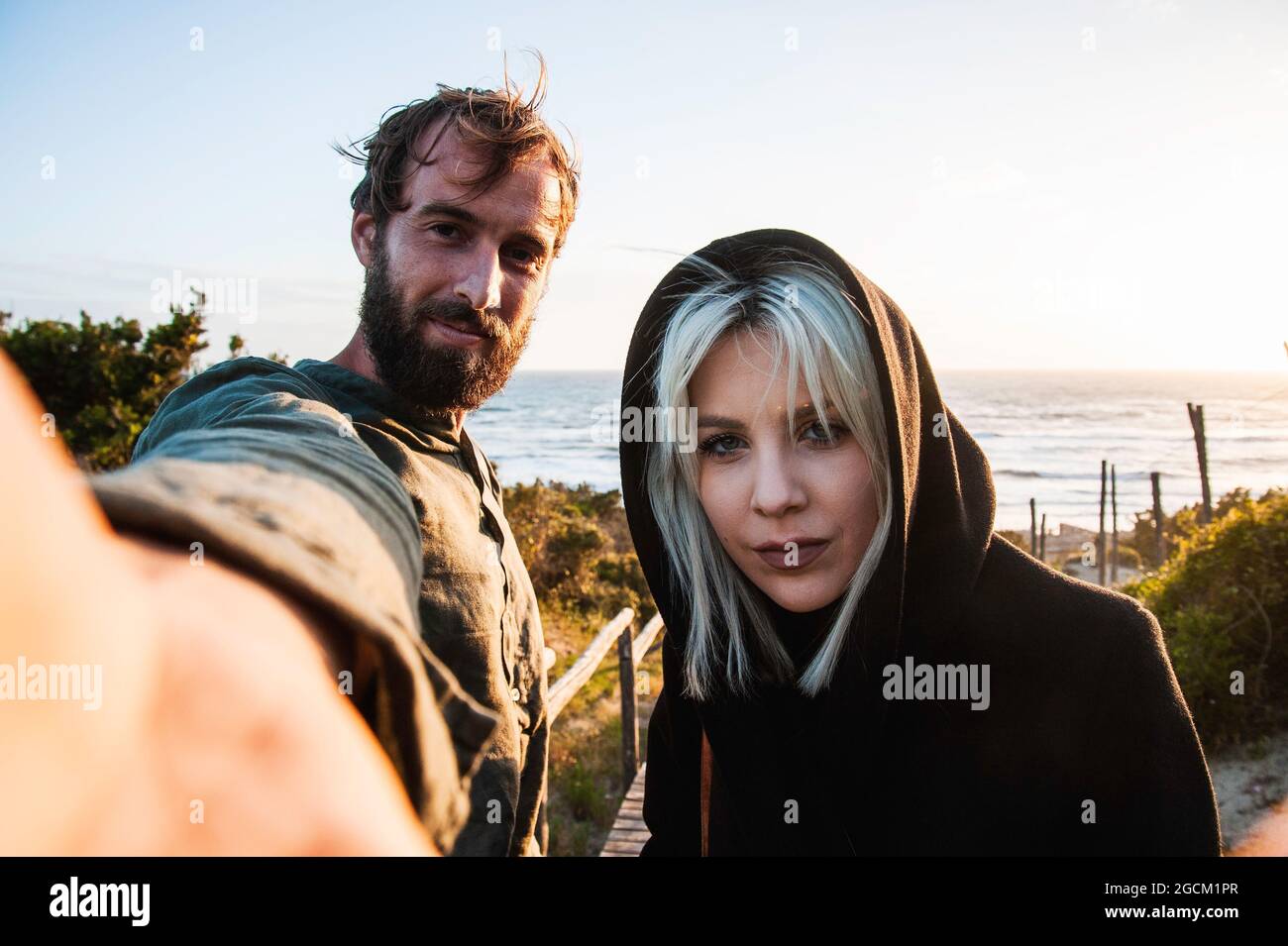 Traveling couple in love taking selfie on the dunes near the beach at sunset - Woman with magnetic gaze and her hipster boyfriend having fun while loo Stock Photo