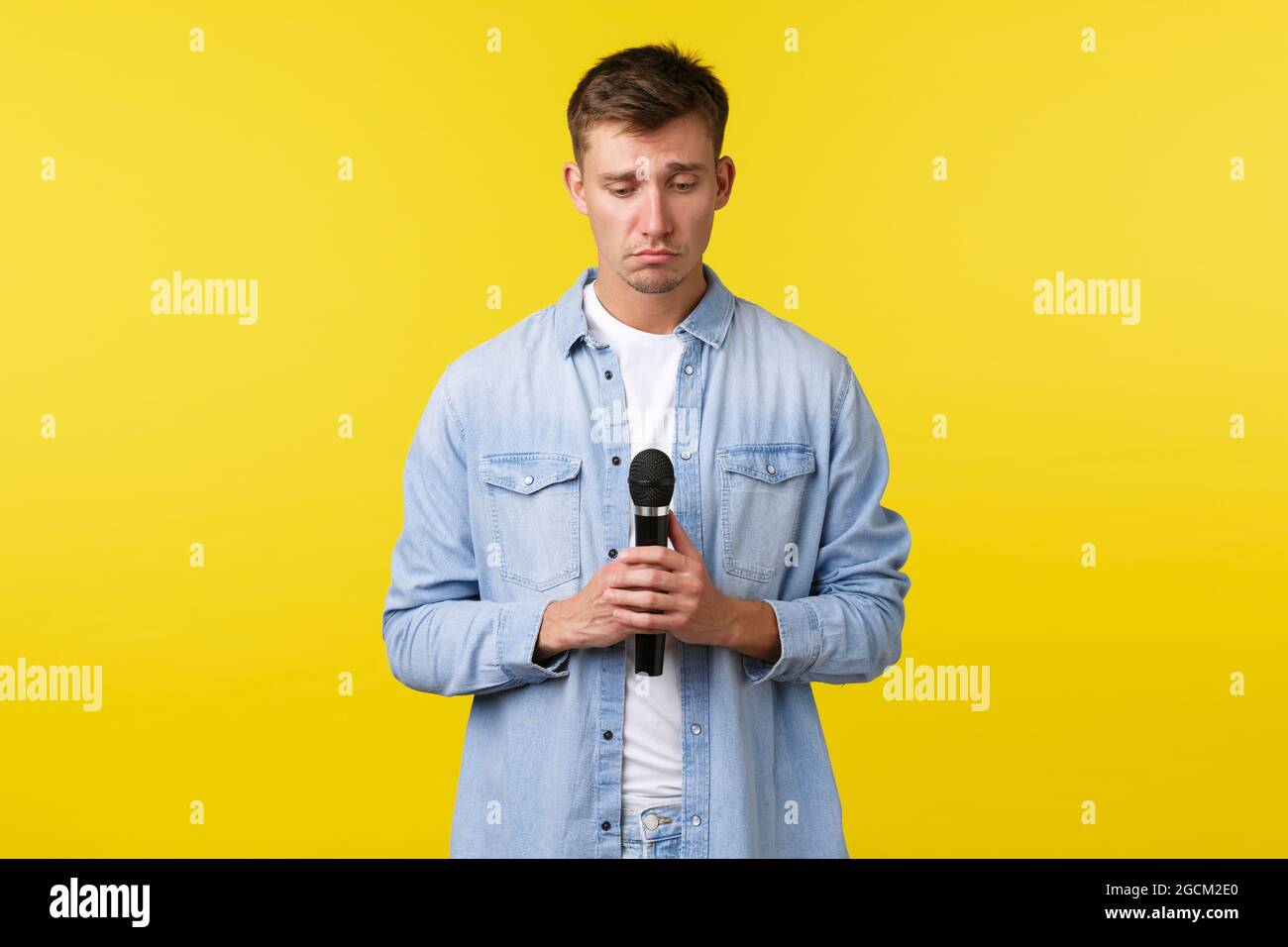 Lifestyle, people emotions and summer leisure concept. Gloomy and grieving, heartbroken blond guy sobbing, looking down uneasy as holding microphone Stock Photo