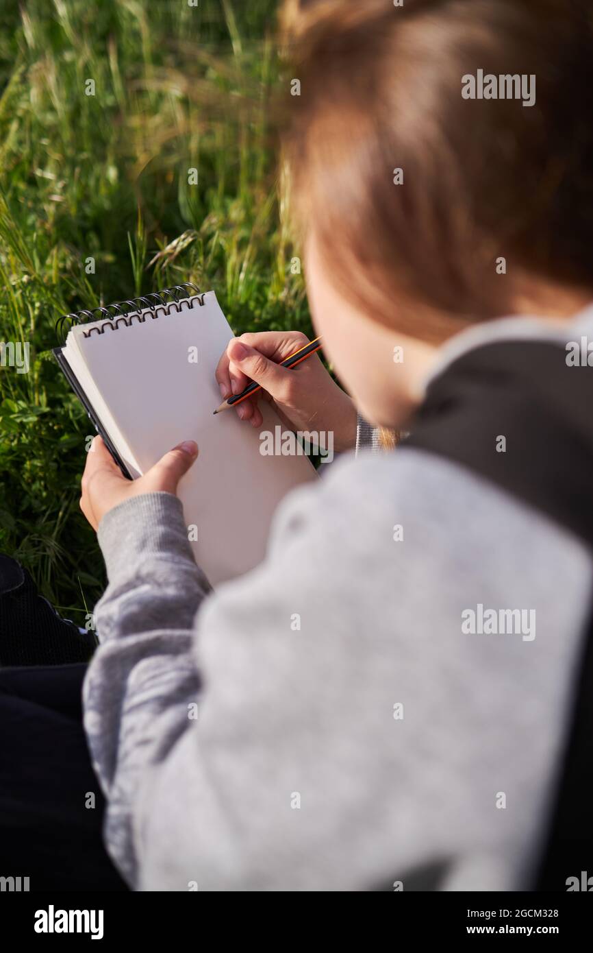 https://c8.alamy.com/comp/2GCM328/back-view-of-unrecognizable-teen-girl-hiding-face-while-sitting-in-meadow-and-drawing-in-sketchbook-enjoying-sunny-day-in-countryside-2GCM328.jpg