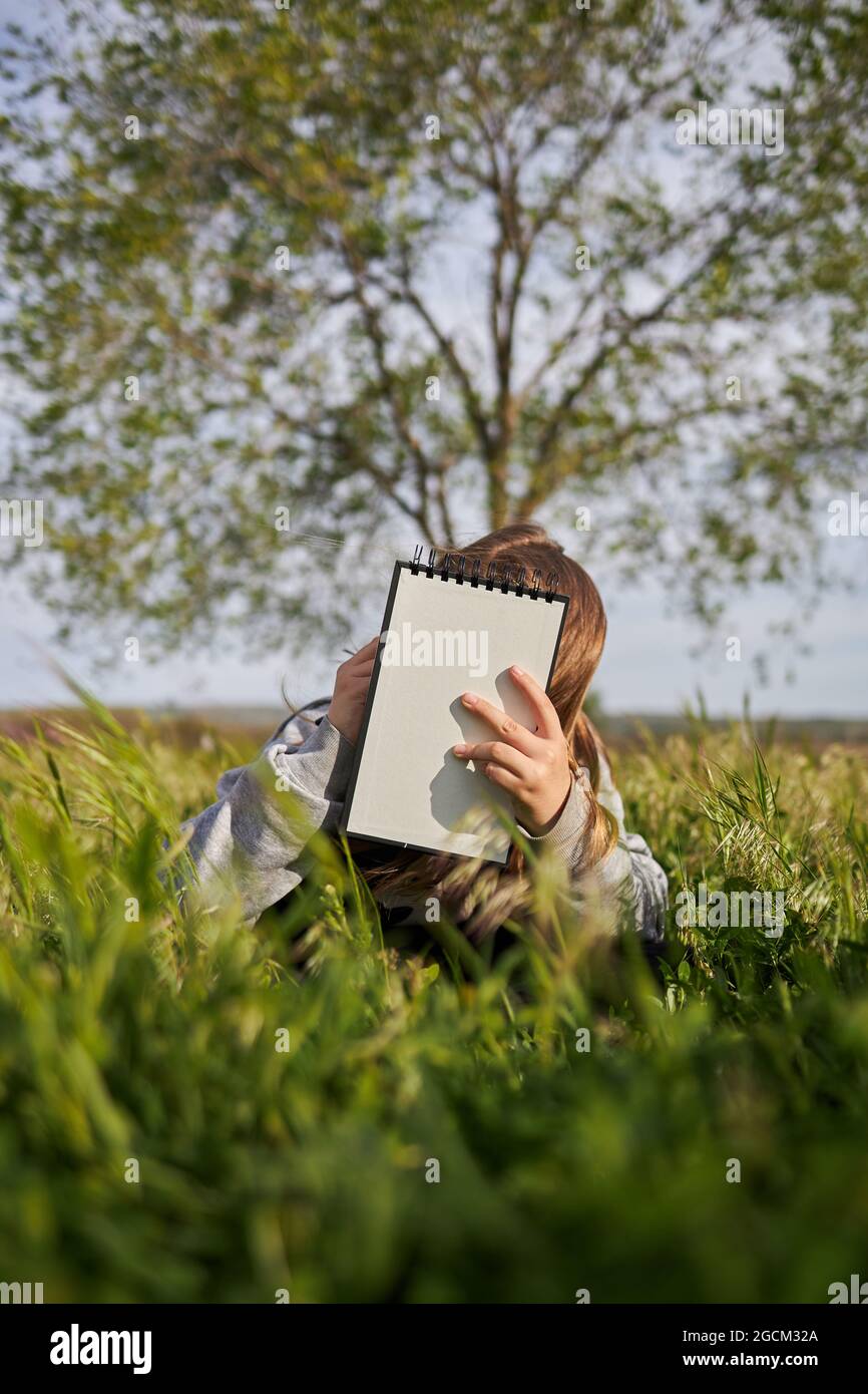 Unrecognizable teen girl sitting in meadow and drawing in