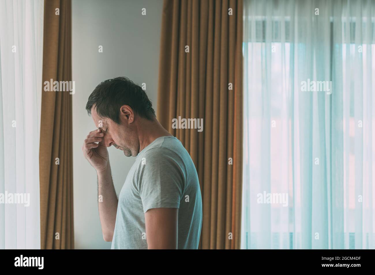 Depressed man is standing by the window. Sad disappointed male person with mental health problems, selective focus. Stock Photo