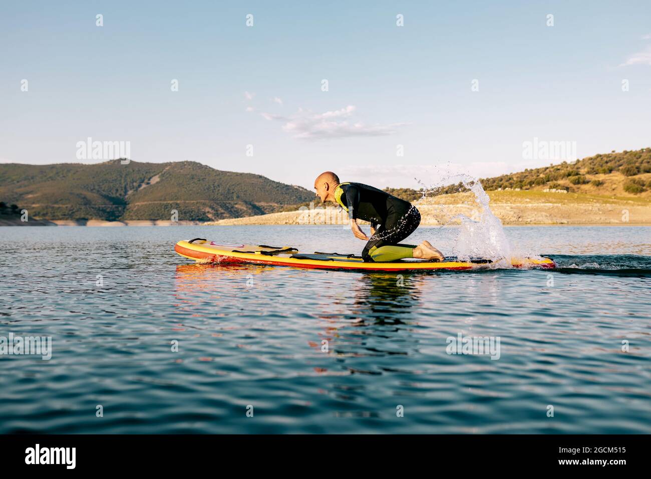 Full body side view of adult male in wetsuit kneeling on paddle board