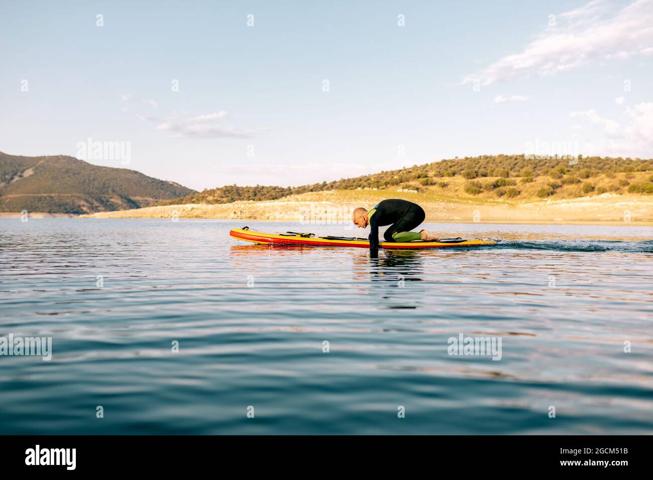 Full body side view of adult male in wetsuit kneeling on paddle board
