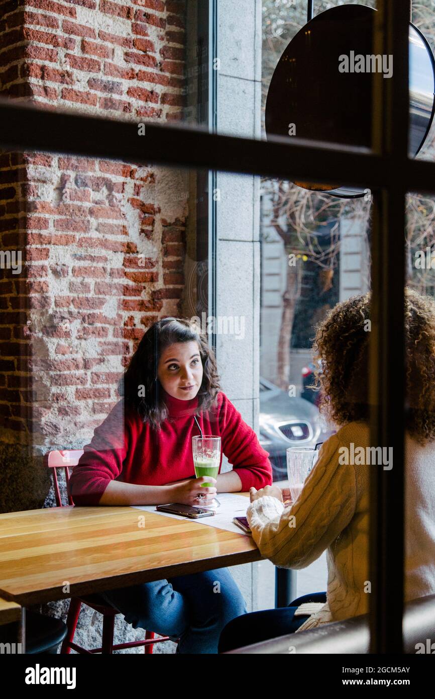 View through a glass of two friends looking at their cell phones inside a bar while having a fruit smoothie Stock Photo