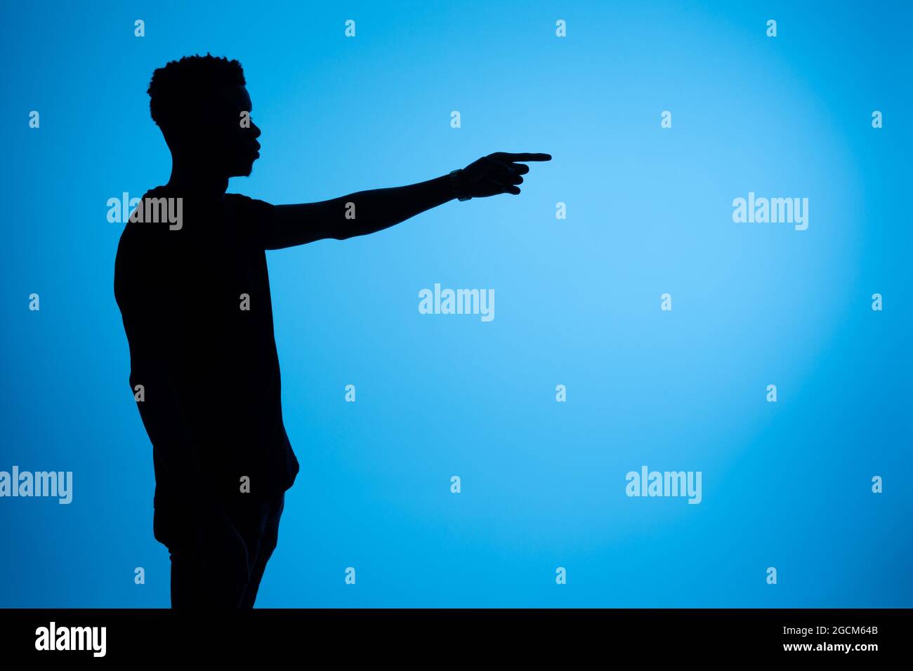 Side view of silhouette of African American male standing with outstretched arm and pointing away on blue background in studio Stock Photo