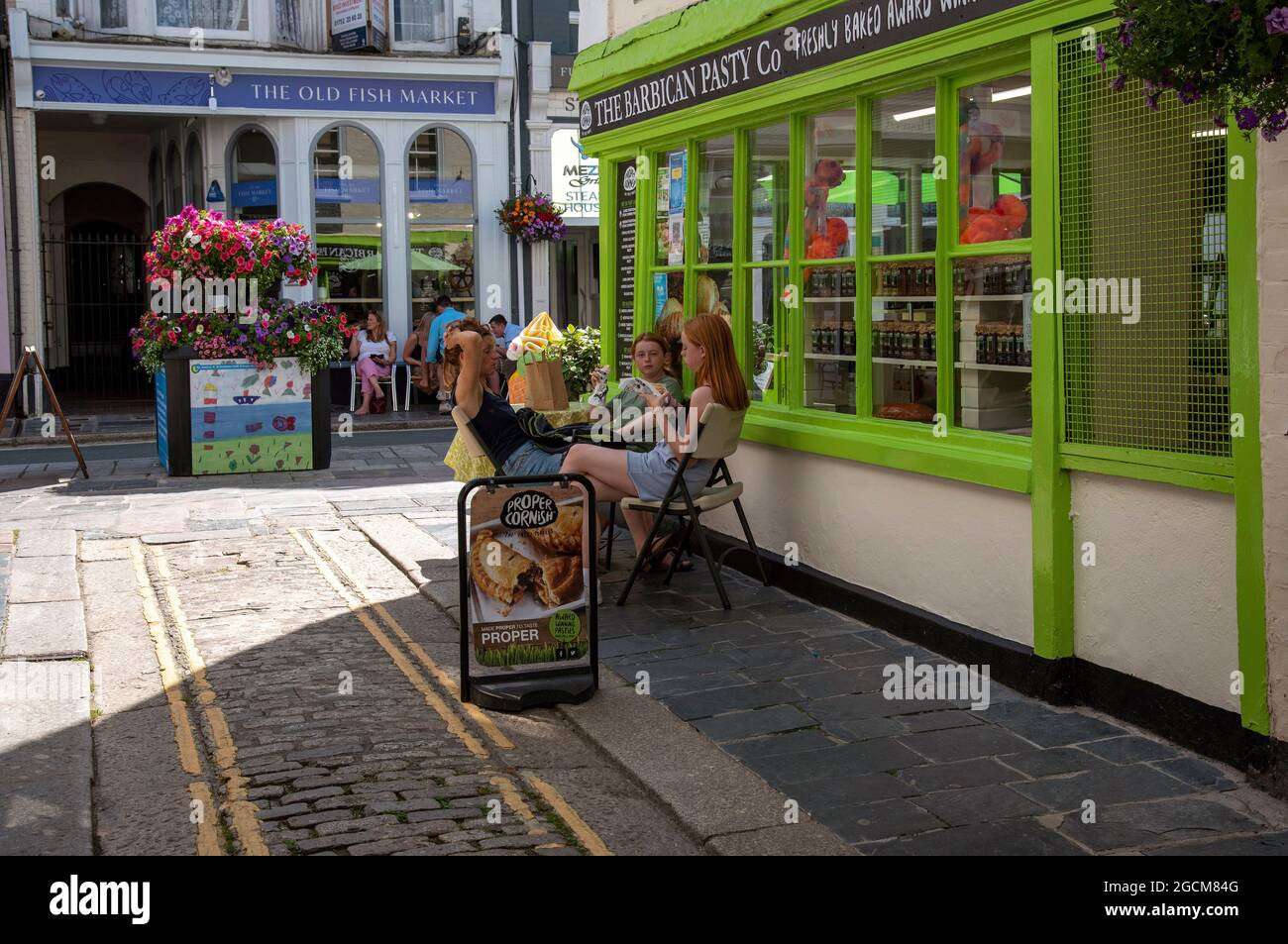 Plymouth, Devon, England, UK. 2021.  Young women eating Cornish pasties in the Barbican area of Plymouth sitting outside  a pasty shop. Stock Photo