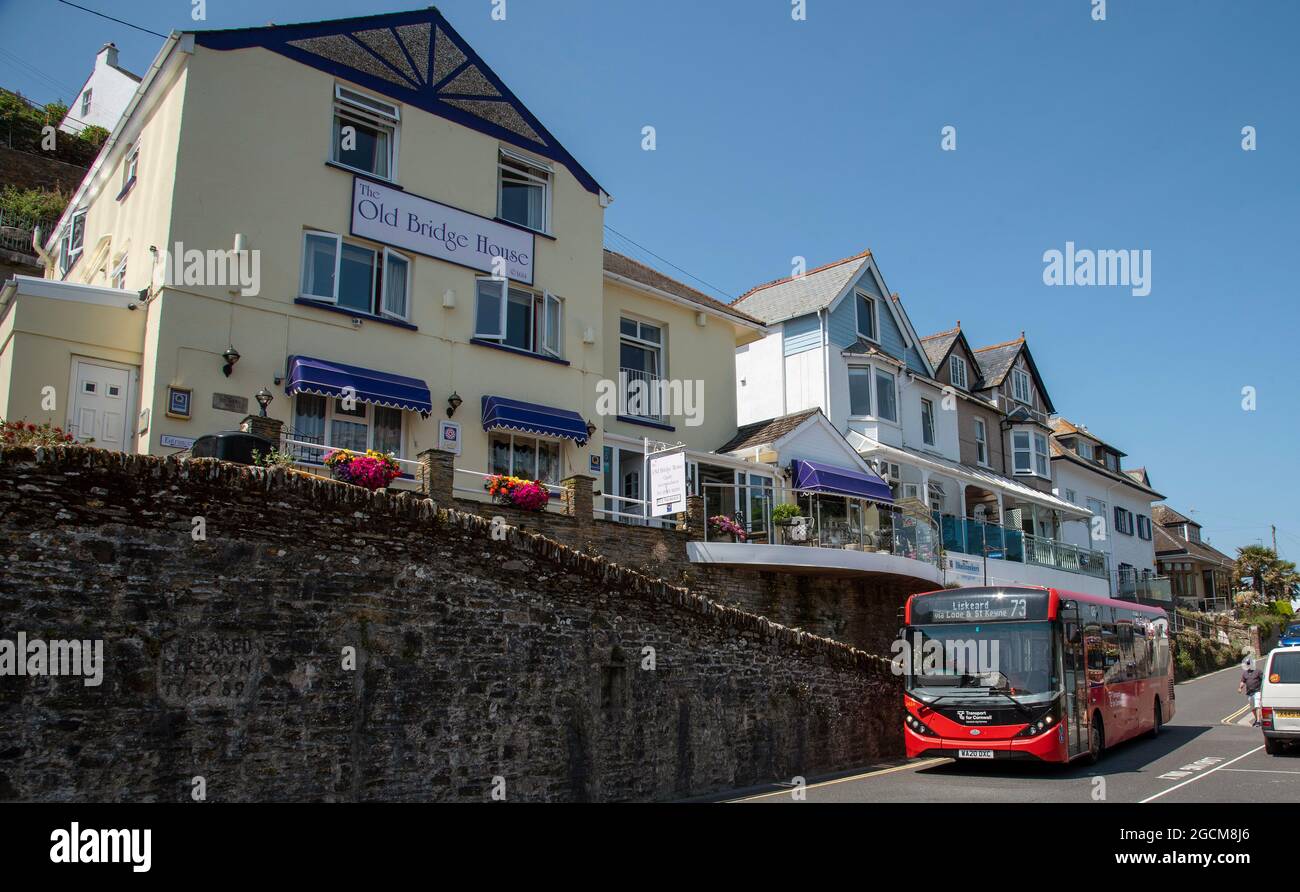 Looe, Cornwall, England, UK. 2021. A red single deck bus passing holiday accommodation in West Looe, UK Stock Photo