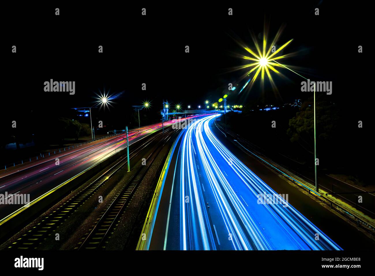 Light trails on a motorway either side of railway tracks at night, Perth, Western Australia, Australia Stock Photo