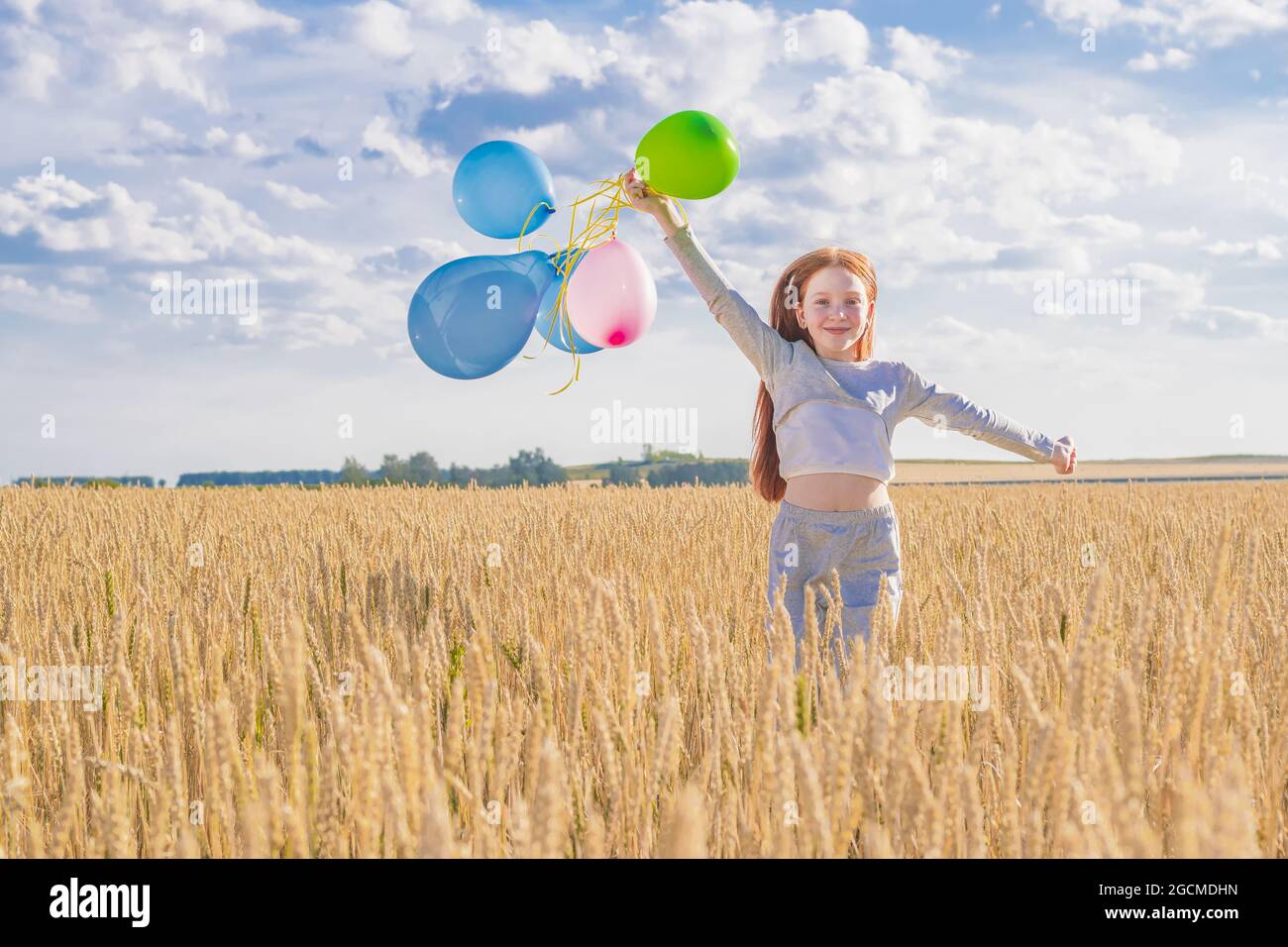 Happy young girl with red hair runs in a wheat field with colorful ...