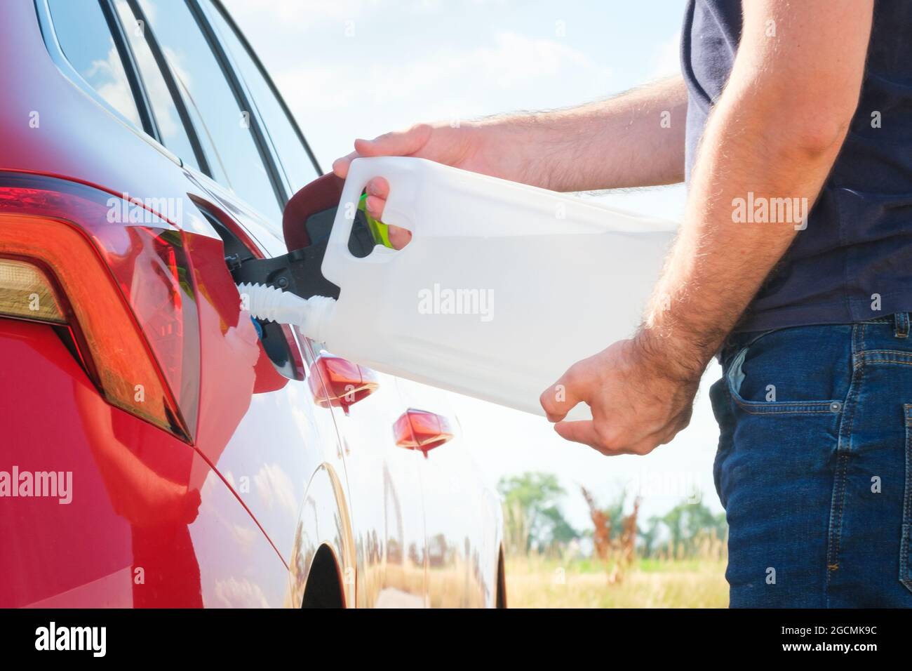 Close up woman refilling the red car with fuel or a diesel engine fluid from canister in the field.  Stock Photo