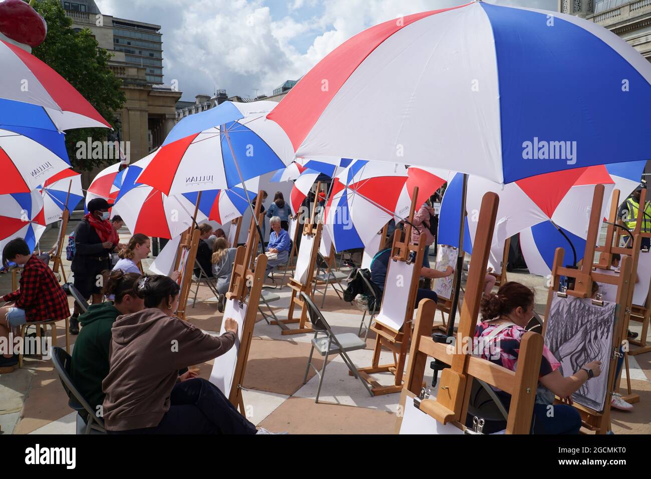 London, UK, 9 August 2021: The National Gallery offers art classes in Trafalgar Square as part of the Inside Out Festival throughout August. Thirty easels have been set up -- with umbrellas for the erratic summer weather -- and people of all ages can drop in to Sketch on the Square for guidance in drawing skills. Anna Watson/Alamy Live News Stock Photo