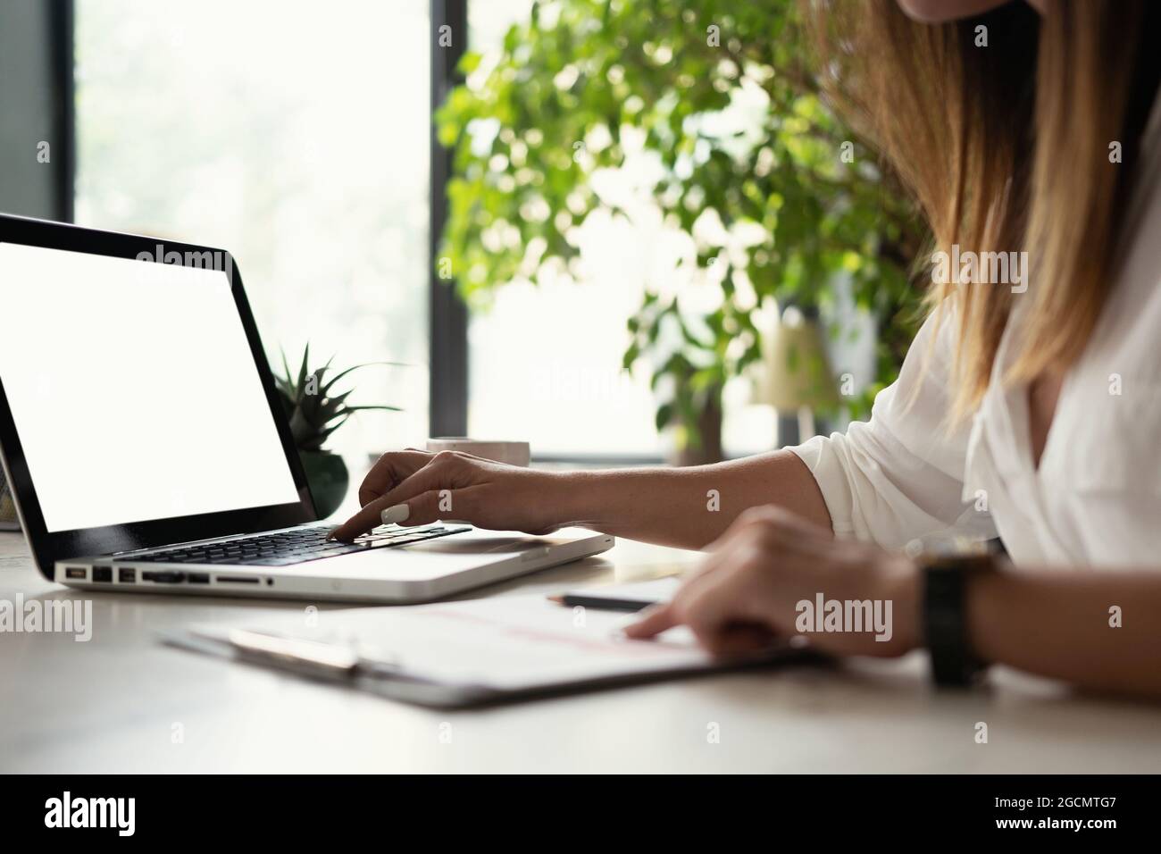 Beautiful Female Data Analyst sitting at the Table Works on a Laptop. Stylish Woman in the Modern Office Environment. Stock Photo