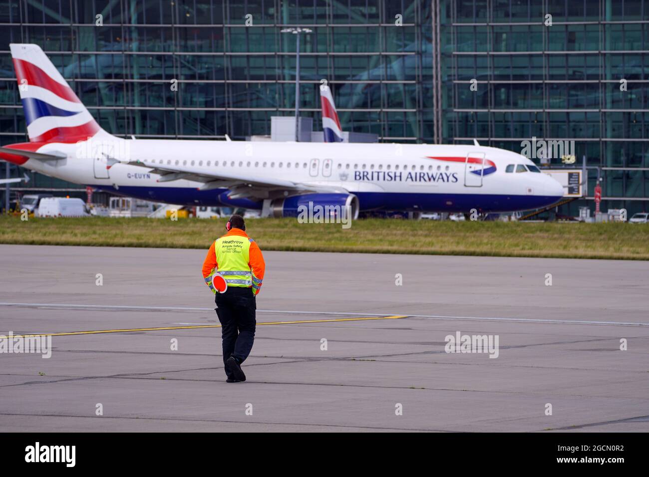 A Heathrow Airside Safety Senior Airfield Officer looks on as an Airbus A320-232 taxies past Terminal 5 at Heathrow Airport, London. Picture date: Friday August 6, 2021. Stock Photo