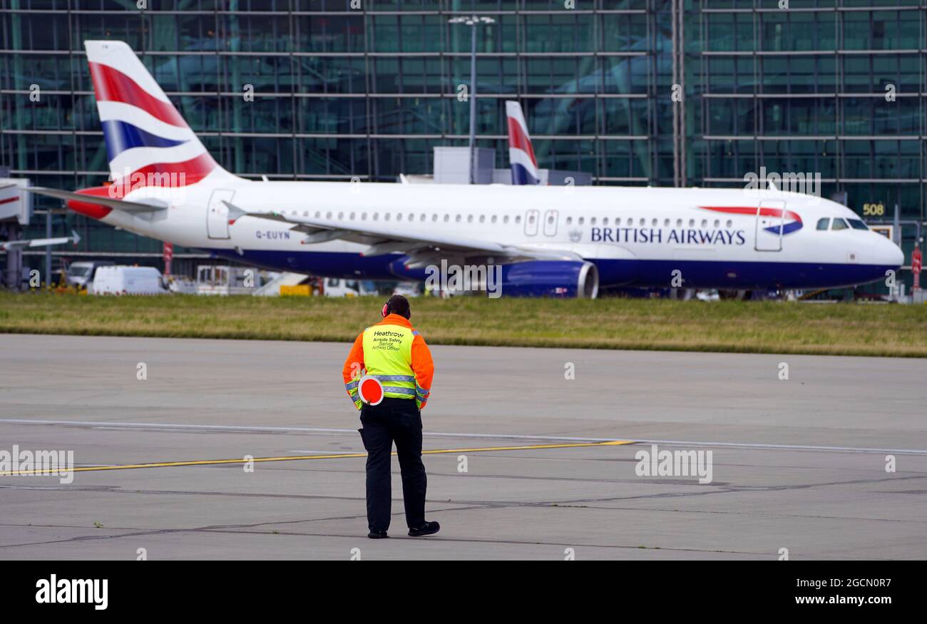 A Heathrow Airside Safety Senior Airfield Officer looks on as an Airbus A320-232 taxies past Terminal 5 at Heathrow Airport, London. Picture date: Friday August 6, 2021. Stock Photo