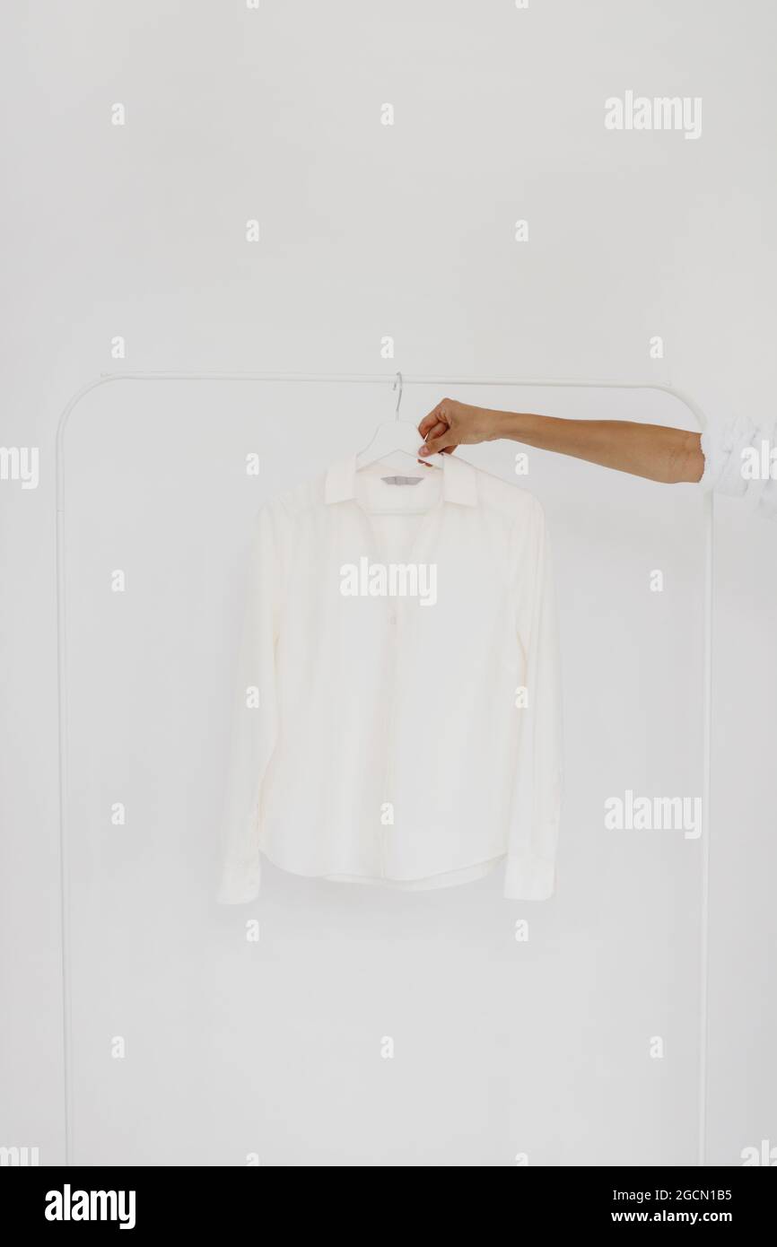 Female hand taking white blouse from hanger on white background. Stock Photo