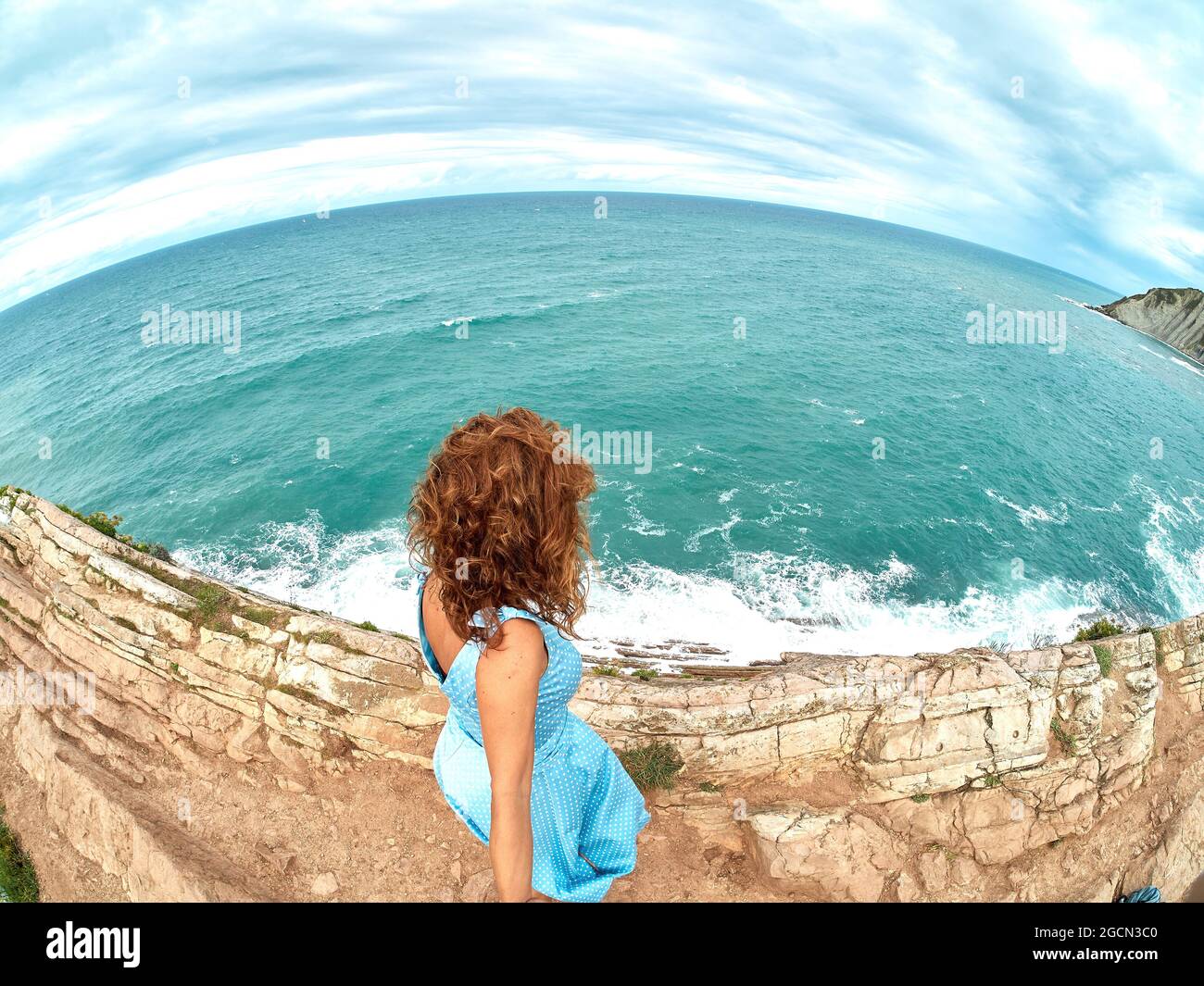 A slim girl in a dress with her back to the sea. A woman is on the beach. Rest in the sea. Fisheim lens Stock Photo