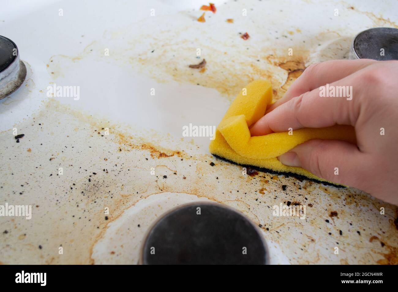 A hand with a yellow wash sponge washes the very dirty greasy surface