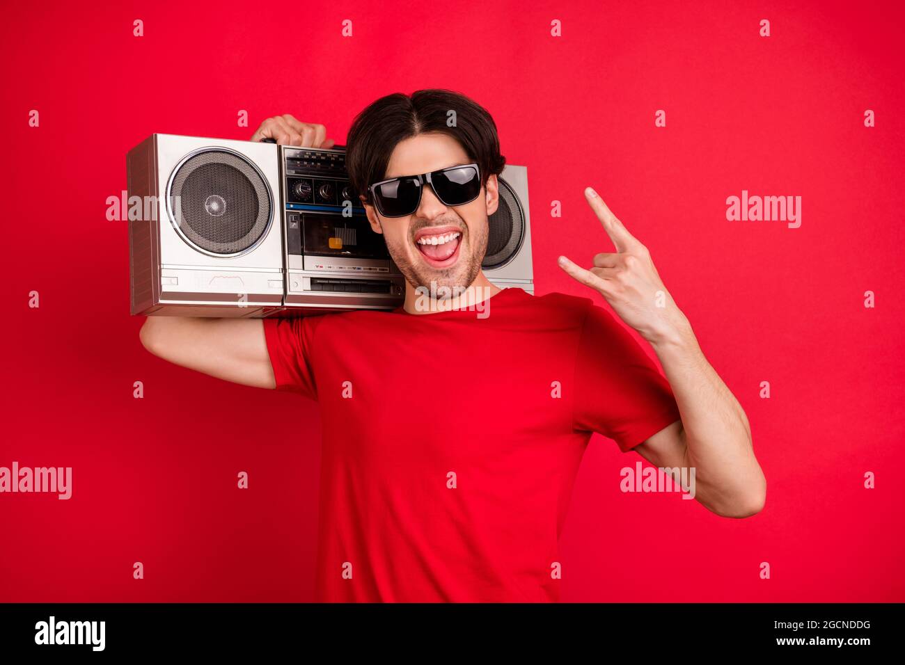 Photo of young excited man show rock sign metal music retro boombox audio isolated over red