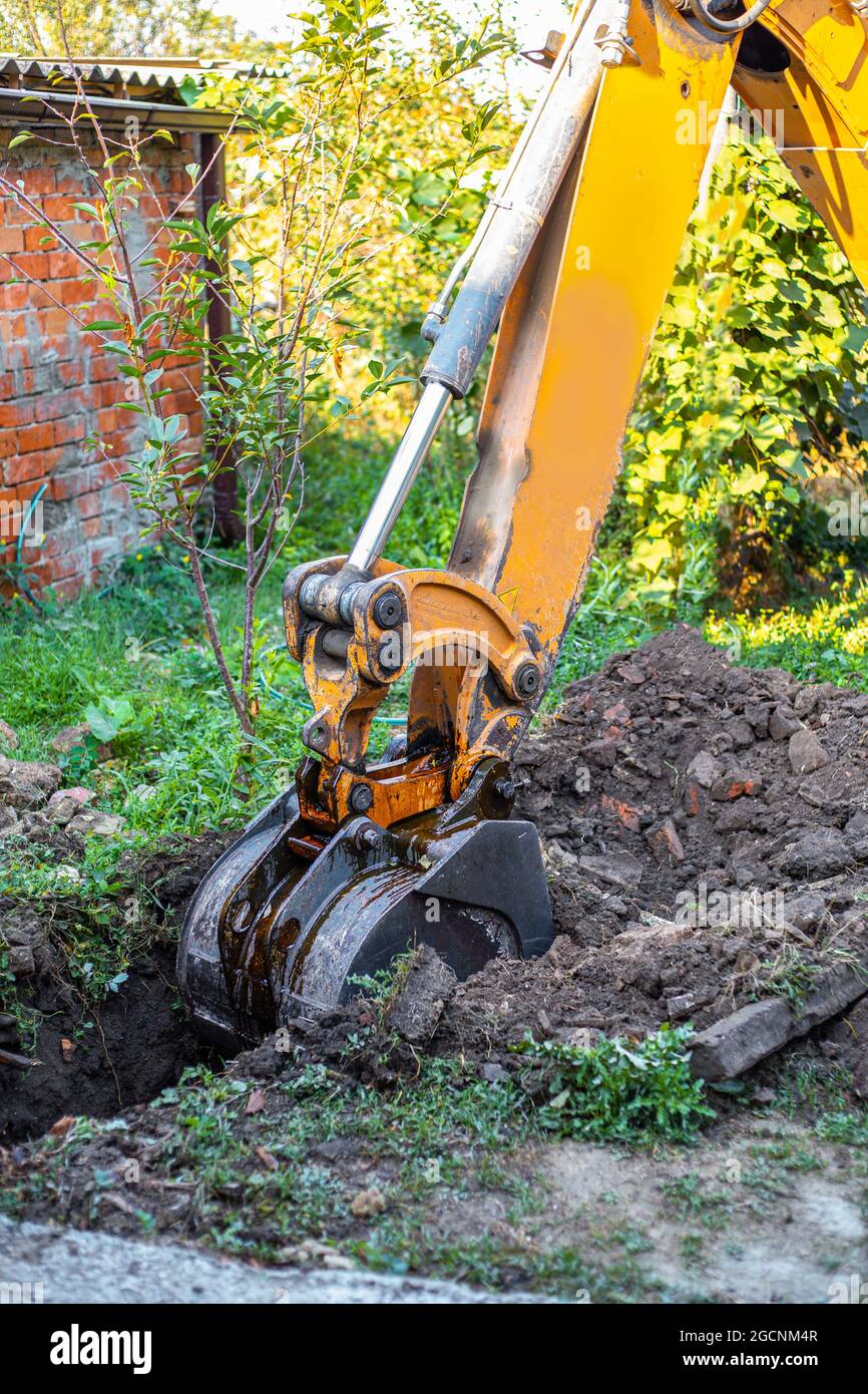 A tractor digs a trench with a bucket to lay a water supply system