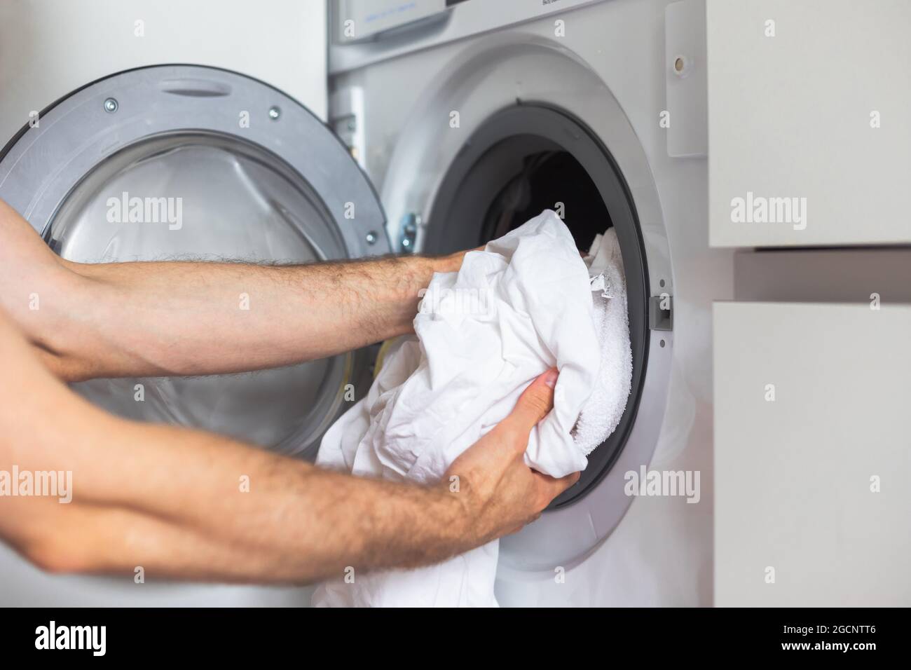 Housework: Man loading white clothes into washing machine Stock Photo