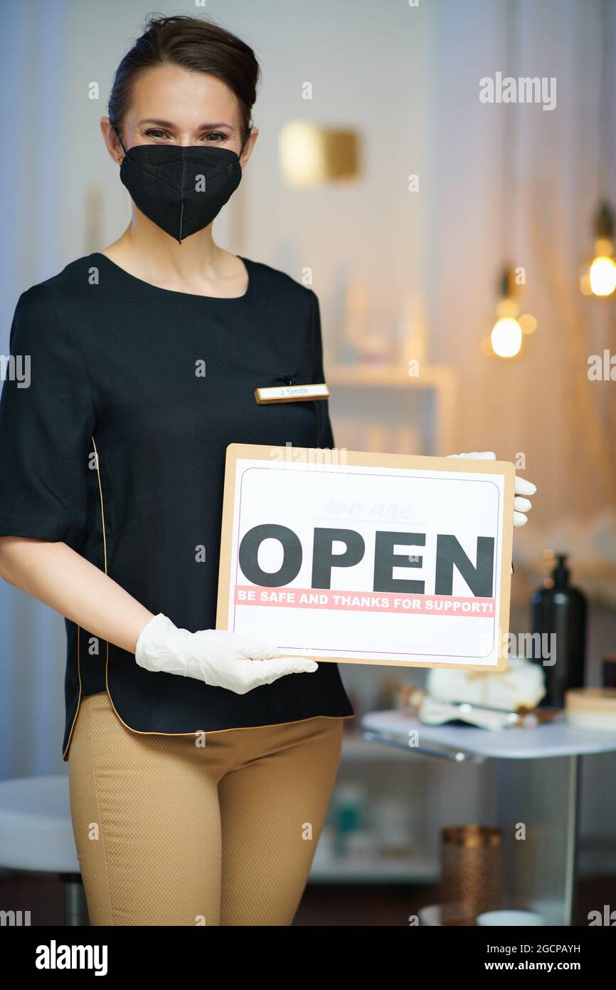 Business during covid-19 pandemic. female employee with ffp2 mask and open sign in modern beauty studio. Stock Photo