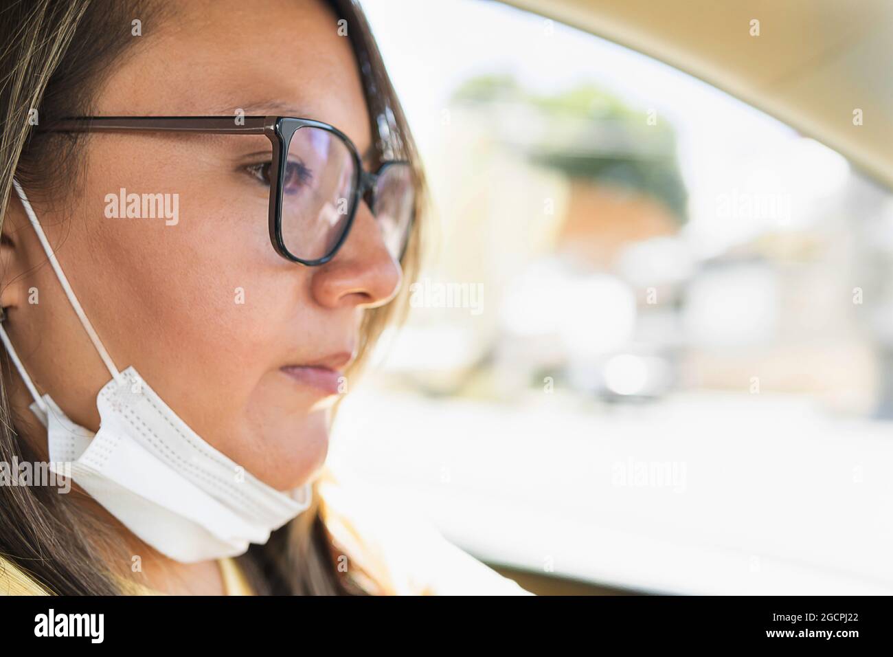 portrait of latin woman with glasses driving with her mask taken off Stock Photo