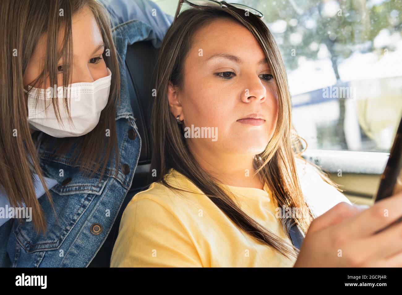 Woman Driving Checking Her Cell Phone While Her Daughter With A Mask