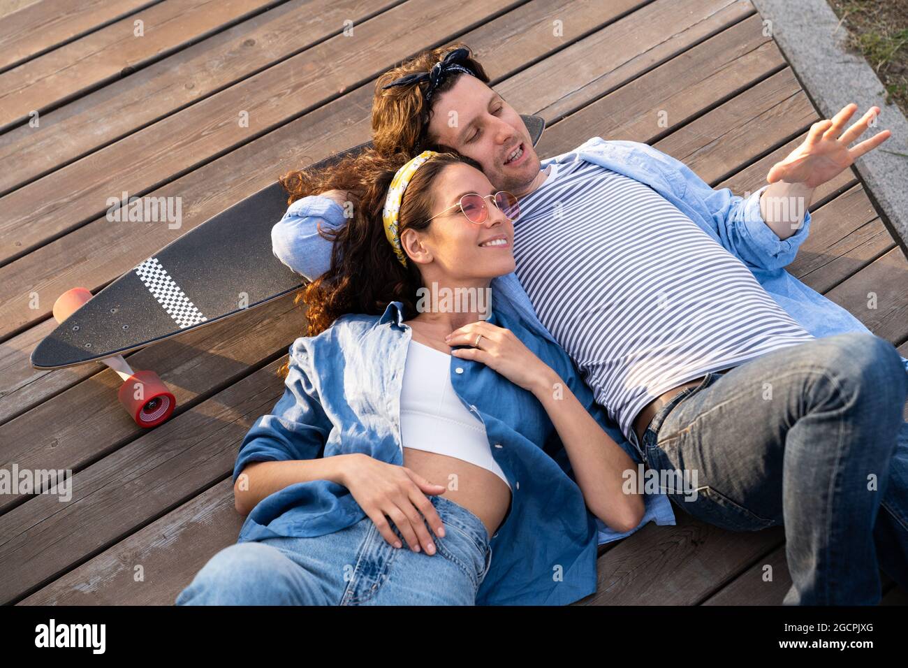 Happy couple of young adults lying on longboard talk enjoying summer sunset. Love and relationship Stock Photo