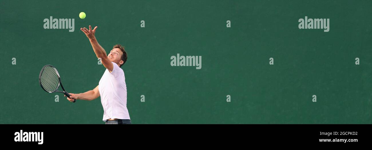 Tennis serve during match. Man tennis player playing throwing ball in the air serving playing on hard indoor court panoramic banner. Stock Photo
