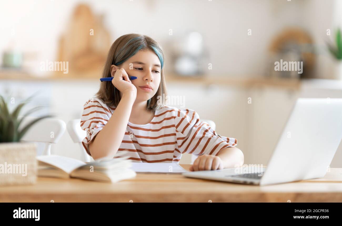 Back to school. Unhappy child is sitting at desk. Girl doing homework or online education. Stock Photo