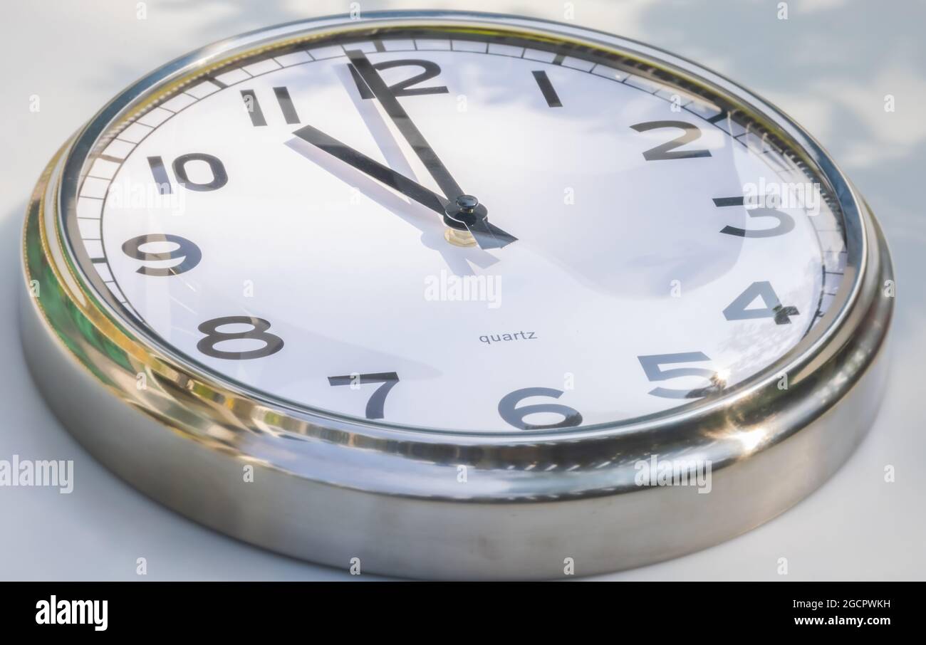 A Modern white aluminum wall clock in sunlight with shadows on the  clock face. Close up to a wall clock. Reflections in the aluminum frame. The point Stock Photo
