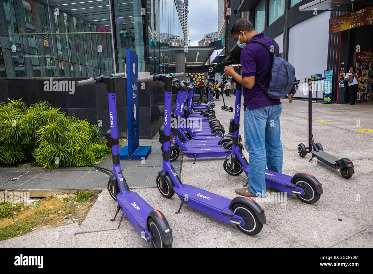 Kuala Lumpur, Malaysia - October 04, 2020: Asian man is booking  public shared electronic scooter from Beam on the roads of Kuala Lumpur. The violet s Stock Photo