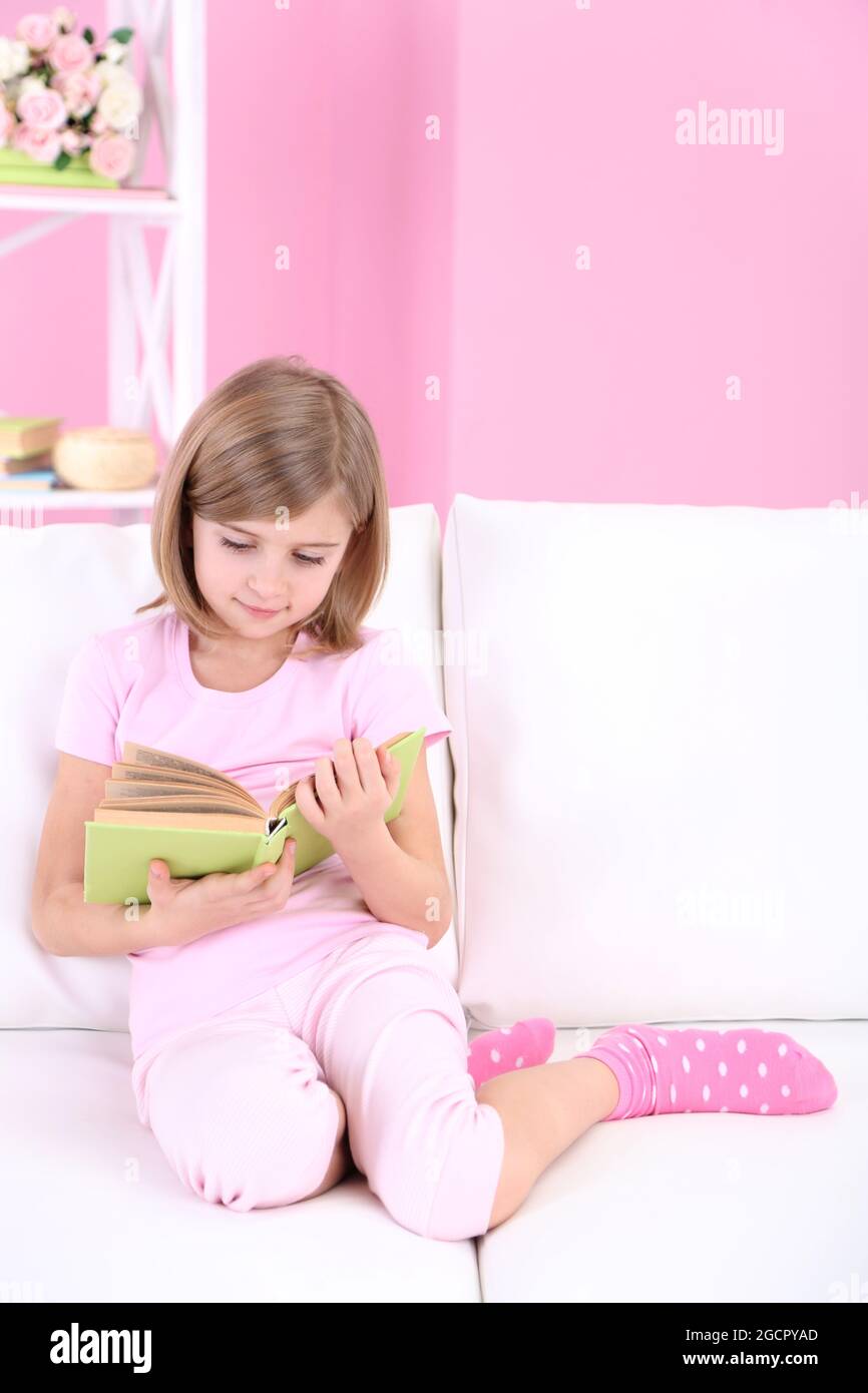 Little girl reading book sitting on sofa in room Stock Photo - Alamy
