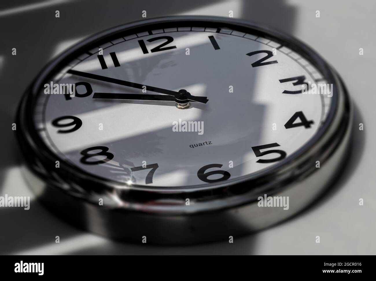 A Modern white aluminum wall clock in sunlight with shadows on the  clock face. Close up to a wall clock. Reflections in the aluminum frame. The point Stock Photo