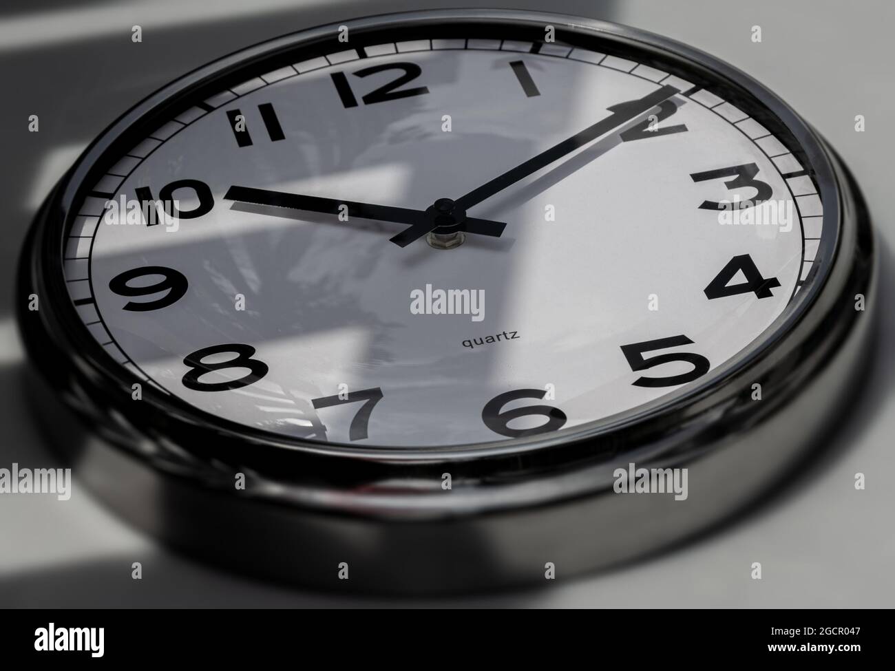 A Modern white aluminum wall clock in sunlight with shadows on the