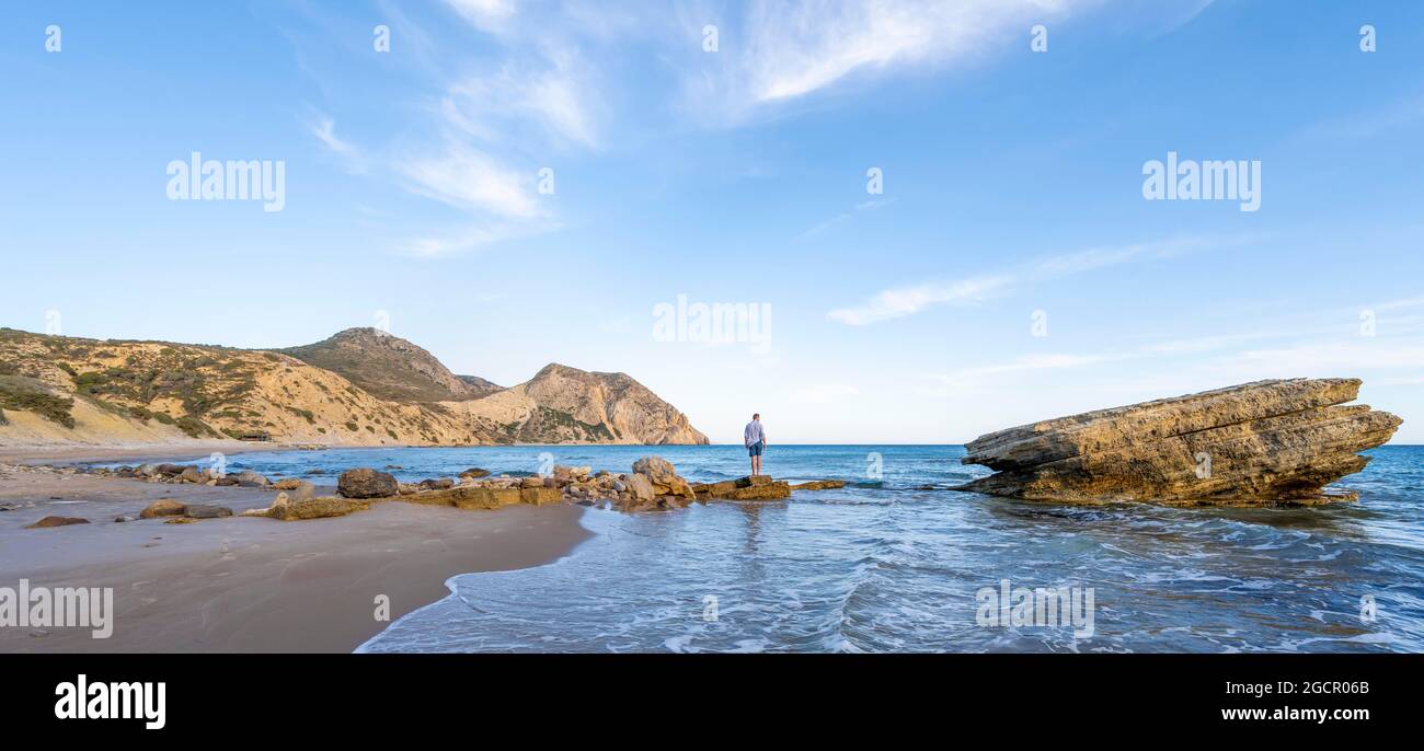 Young man standing on a rock, sandy beach with rocky cliffs, Paralia Paradisos, Kos, Dodecanese, Greece Stock Photo