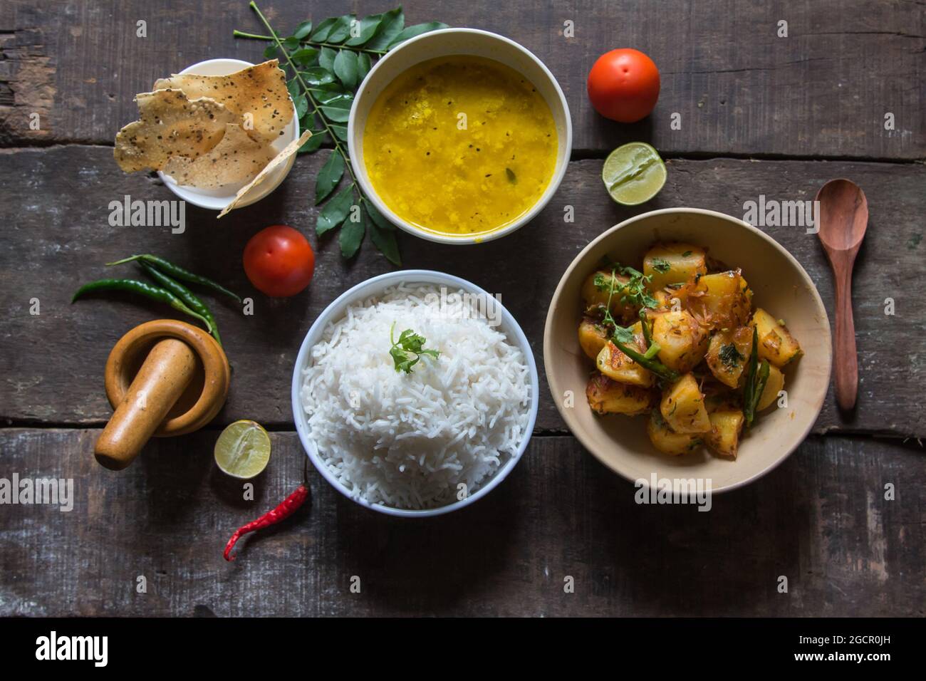 View from top of simple Indian food or meal with potato fry, rice, lentils, papad and condiments. Vegetarian dish. Stock Photo