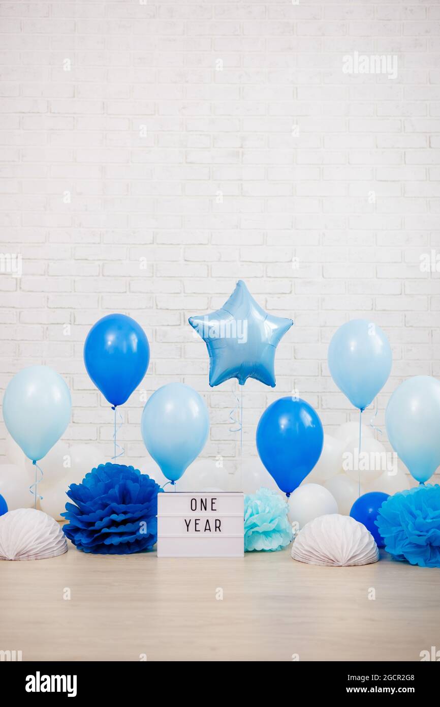 baby boy first birthday party decoration - air balloons, paper balls,  lightbox with one year text and copy space over white brick wall background  Stock Photo - Alamy