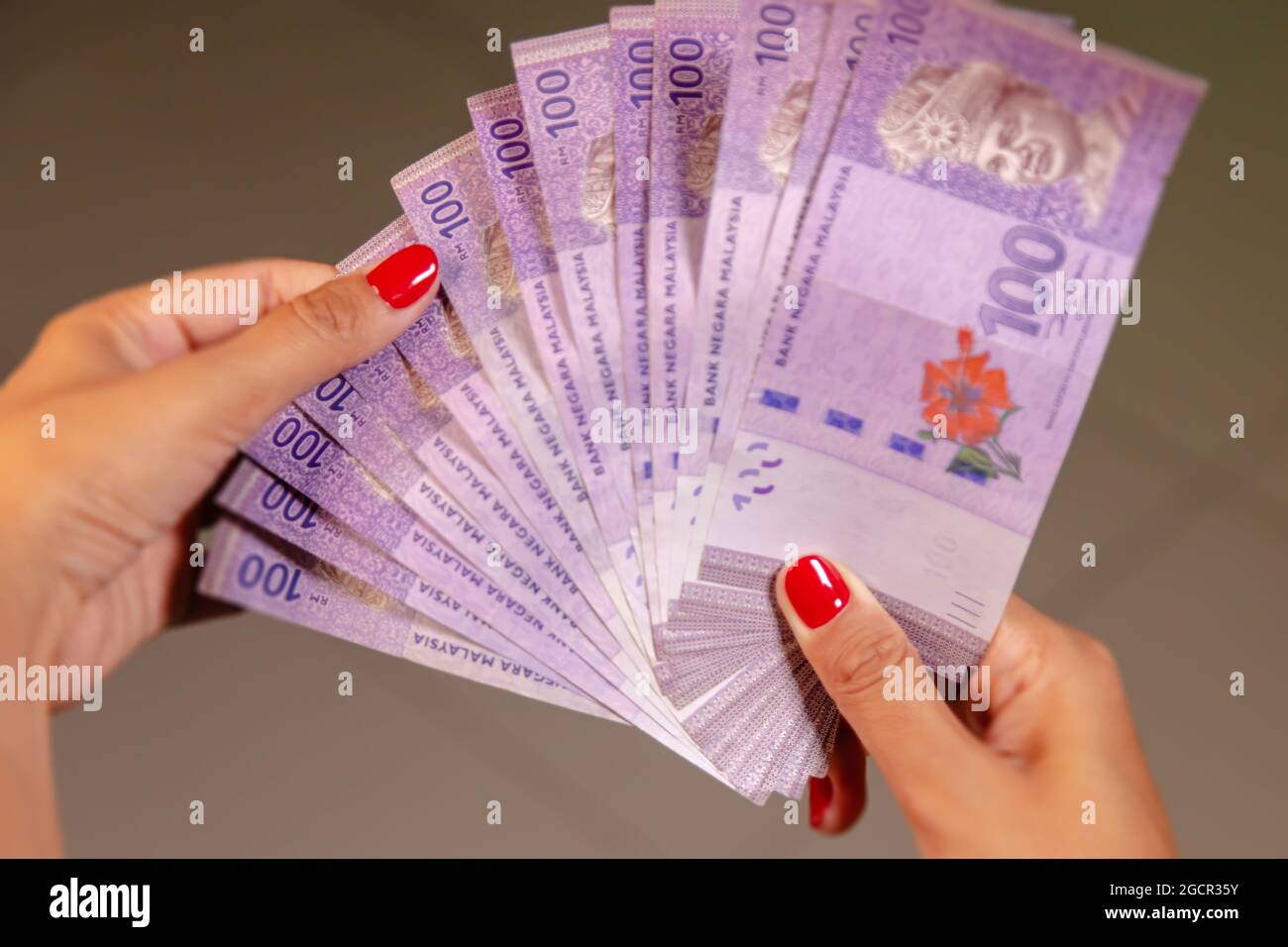 Female Hands with red nails counting 100 Ringgit banknotes. Ringgit the currency of Malaysia. Woman hands showing RM100 notes. Close up to the Malaysi Stock Photo