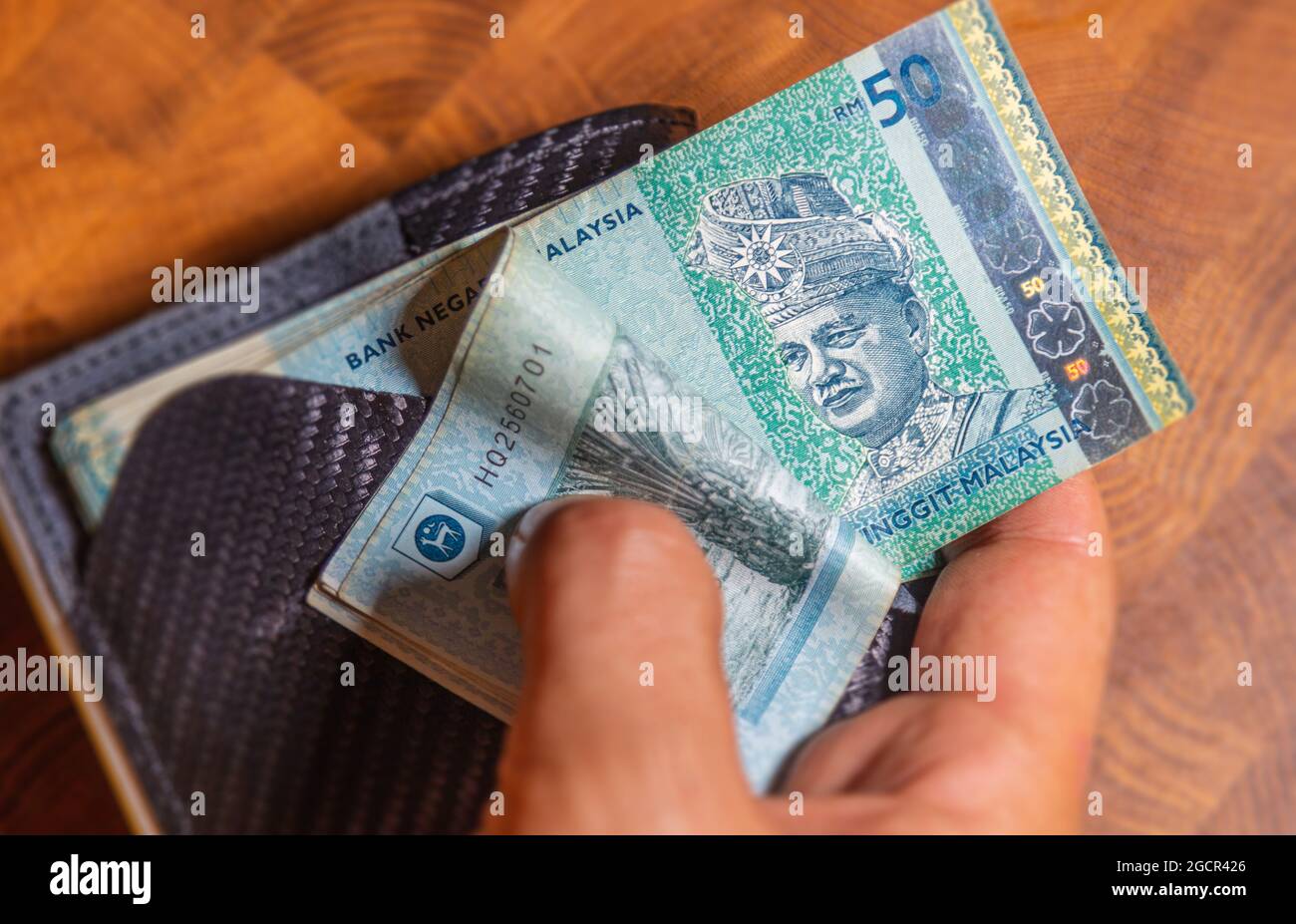 Male hands counting 50 Ringgit Malaysia in a leather wallet on a wooden table. RM50 in mans hand. Malaysian Ringgit shown by young man in a wallet. Cl Stock Photo