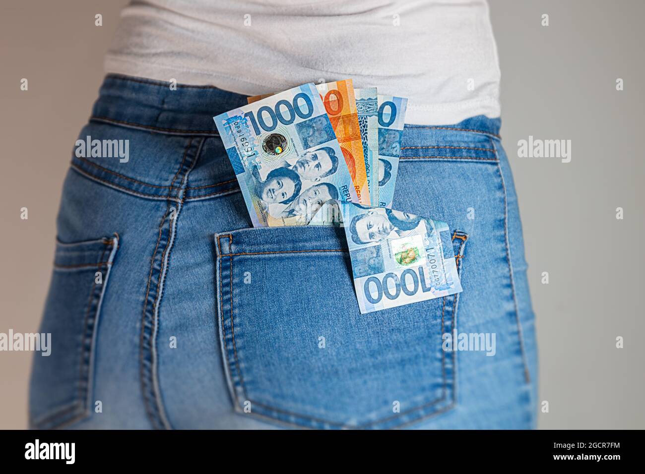 Philippines Peso in a female jeans pocket. Philippine pesos notes stuck in a woman jeans pocket. Pesos in a girl's denim pants buttock pocket. Money i Stock Photo