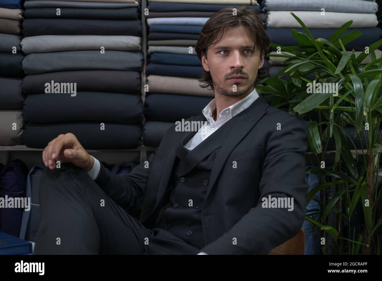 Handsome man in black suit sitting in atelier and looking aside. Serious eyes. High quality photo Stock Photo