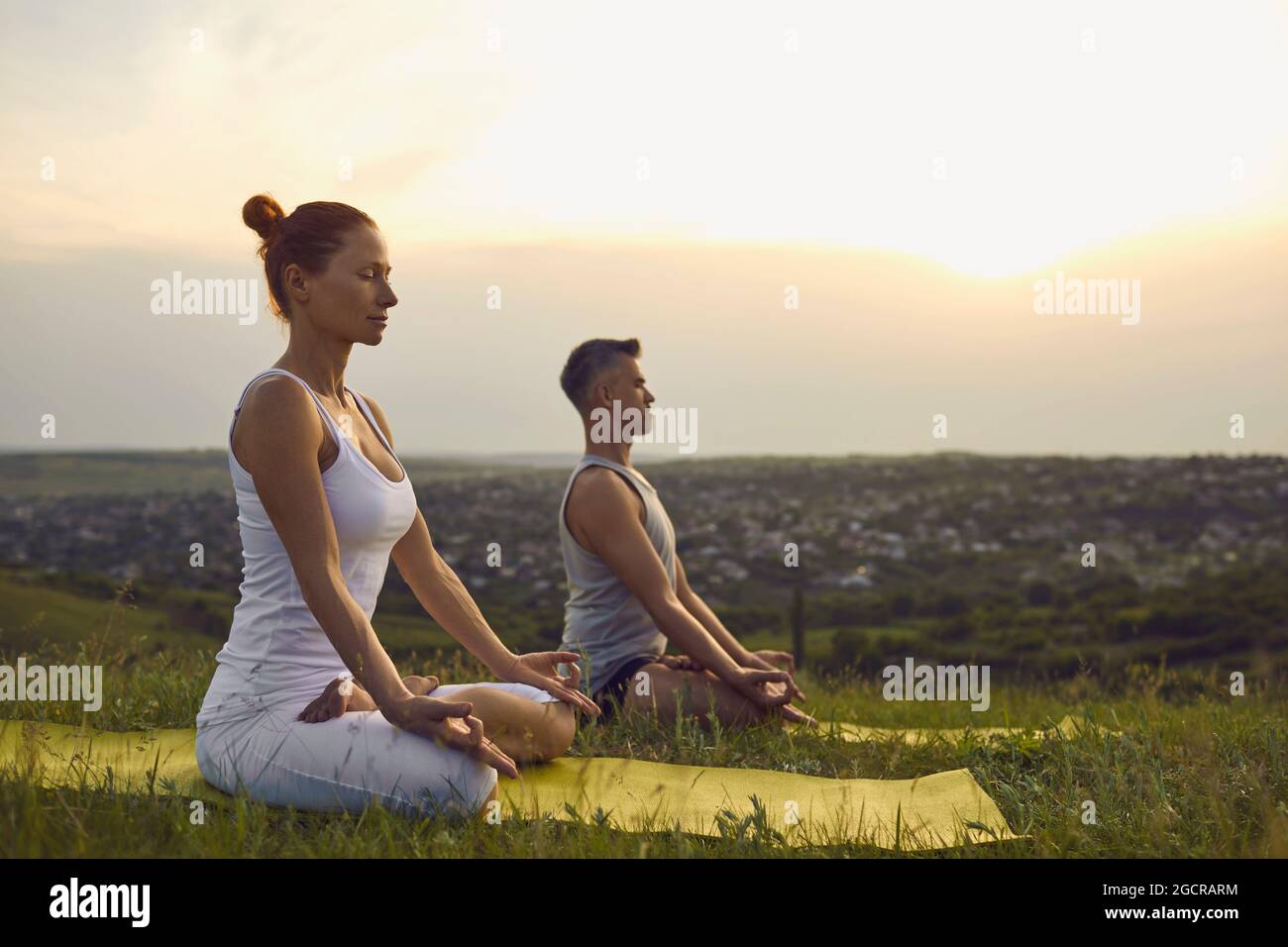 Man and woman meditating outdoors at sunset sitting in Lotus position and breathing deeply Stock Photo