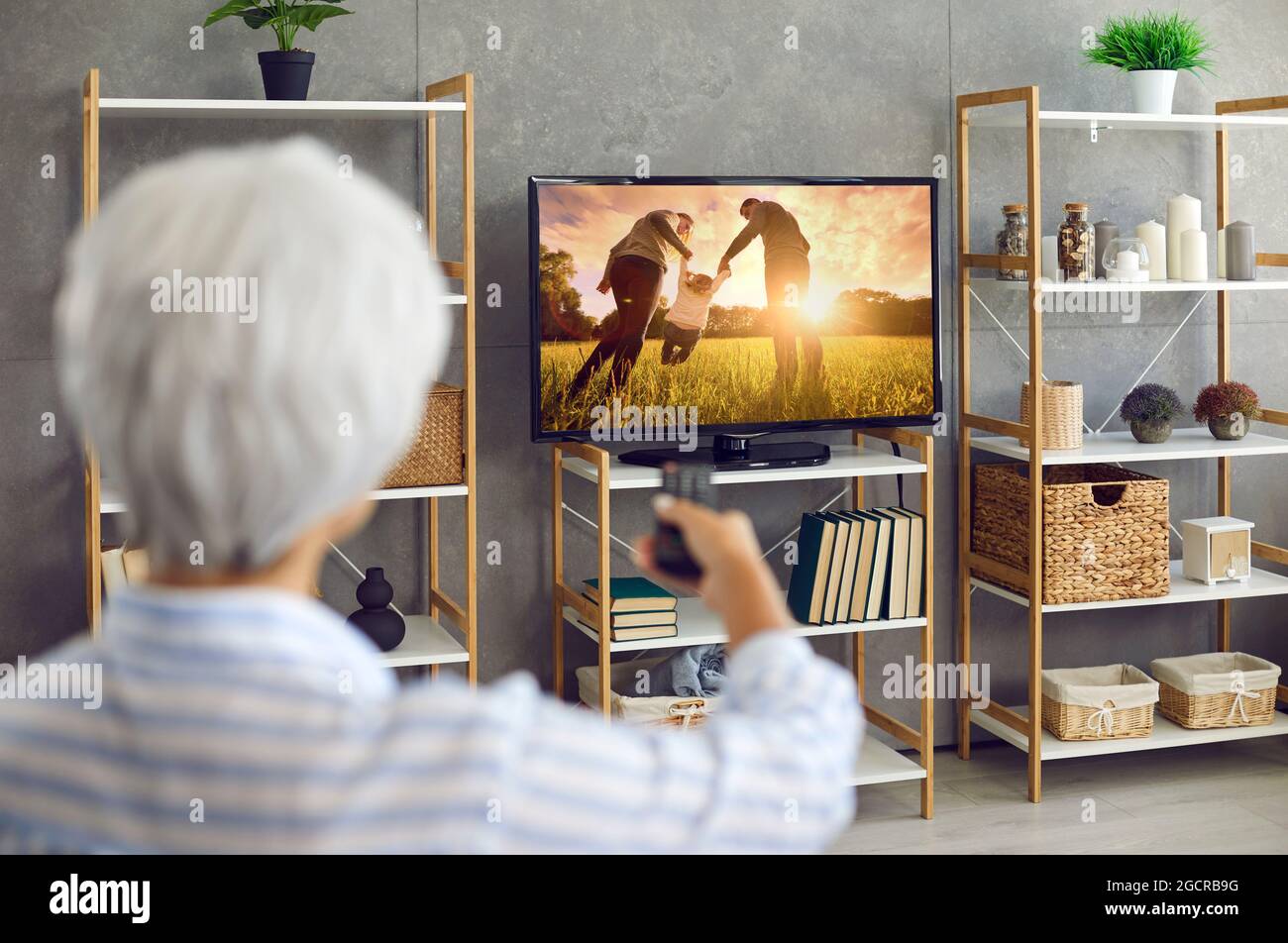Senior woman watching a movie or a TV show on a large modern television set at home Stock Photo
