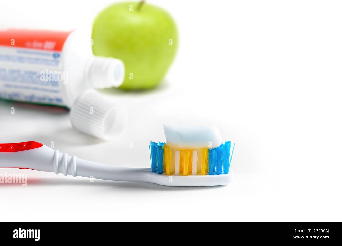 Toothbrush with squeezed paste closeup, tube of toothpaste and green