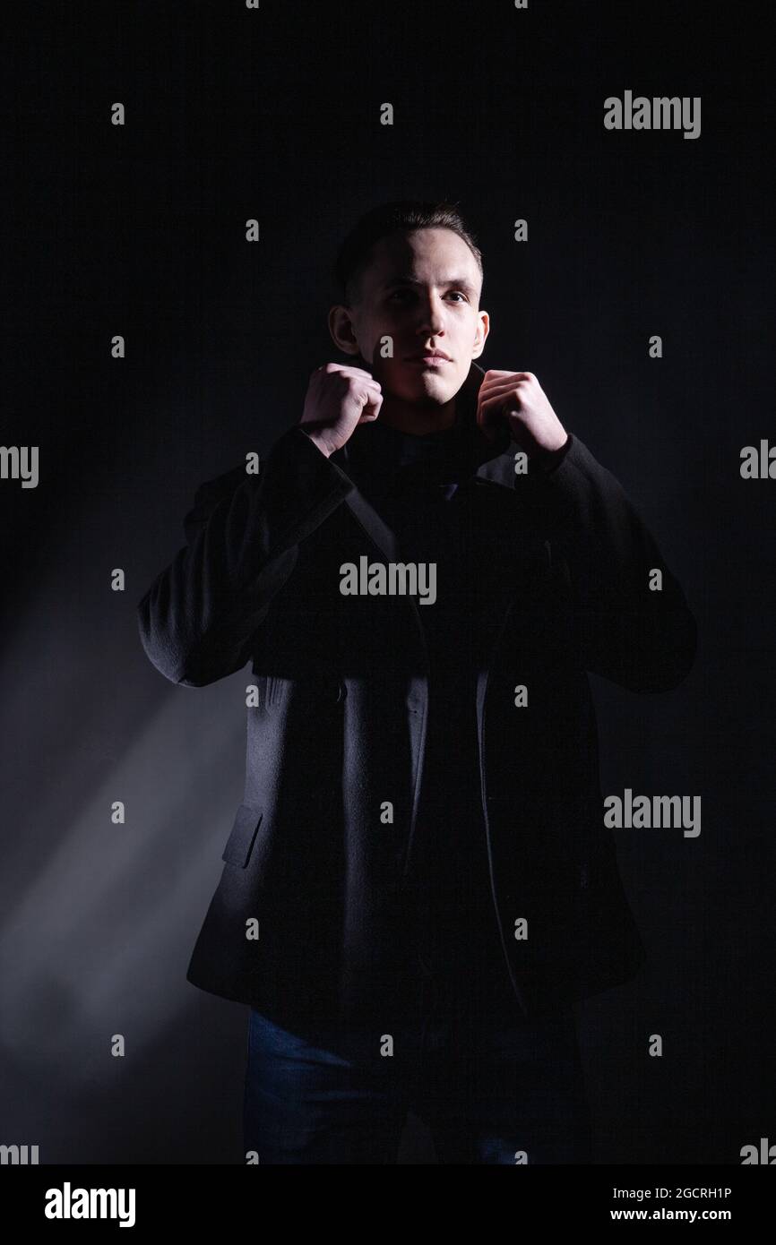 Stylish man in black coat in dark studio Stock Photo