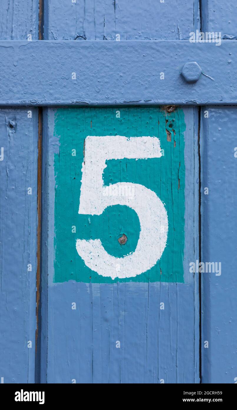 White Number 5 painted on blue and turquoise weathered wooden door Stock Photo
