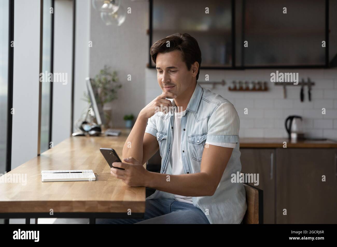 Happy thoughtful millennial guy using app, online service on smartphone Stock Photo